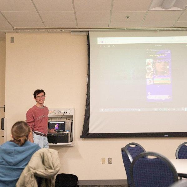 Caleb White stands to the left of a projection screen that shows a Spotify screenshot of Taylor Swift.